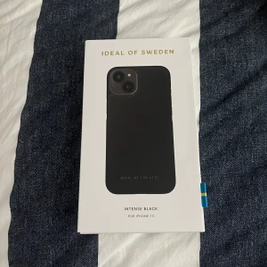 Svart mobilskal från iDeal of Sweden för iPhone 13 - Snyggt och stilrent svart mobilskal från iDeal of Sweden, modell Intense Black, som passar till iPhone 13. Skalet har en slät yta och är designat för att skydda mobilen samtidigt som det ser elegant ut. Helt nytt och oöppnat