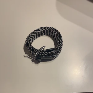 Flätat bälte - Säljer ett snyggt svartvitt flätat bälte med silverfärgat spänne och svarta skinn-detaljer vid ändarna. Bältet har ett coolt zigzag-mönster och passar perfekt till jeans eller chinos.