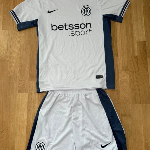 Vit Inter fotbollströja från Nike - Säljer en vit Inter fotbollströja från Nike med mörkblå detaljer och klubbmärke på bröstet. Tröjan har korta ärmar och sponsortryck på framsidan. Materialet är lätt och andas, perfekt för match eller träning.