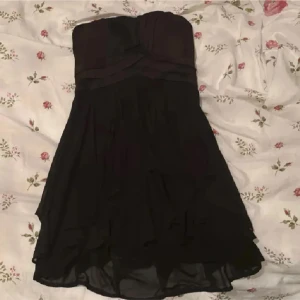 Svart axelbandslös klänning - Säljer en svart axelbandslös klänning med draperad överdel och lätt volang i kjolen. Klänningen har en luftig känsla och är perfekt för festliga tillfällen❤️ Supersnygg