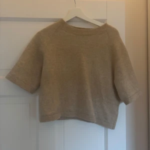 Beige stickad trekvarts tröja från & Other Stories - Säljer en beige stickad tröja från & Other Stories. Tröjan har korta ärmar och en rund halsringning med ribbad kant. Perfekt för lager-på-lager och enkel att matcha med olika outfits.