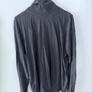 Svart polotröja från Punter Active Wear - Svart långärmad polotröja från Punter Active Wear med trycket 'AnnonsKraft' på kragen. Tröjan är i ett mjukt material och har en klassisk passform med hög krage. Perfekt för en stilren och enkel look.