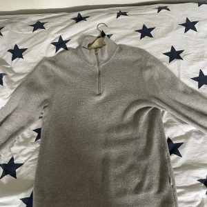 Jack and Jones half zip - Säljer en ljusgrå stickad tröja med hög krage och halv dragkedja framtill. Tröjan har lång ärm och är perfekt för kyligare dagar. Enkel och stilren design som passar till mycket.