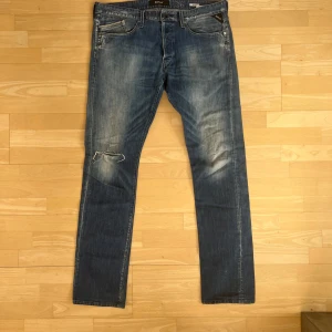 Blå Replay jeansbyxor herr - Säljer ett par klassiska blå Replay jeans med raka ben och snygga slitningar. Byxorna har fem fickor, dragkedja och knapp i midjan samt Replay-logga på bakfickan. Perfekta för en avslappnad stil.