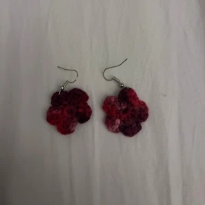 Rosa och röda virkade blomörhängen - Säljer ett par handgjorda virkade örhängen i form av blommor i olika nyanser av rött och rosa. Perfekta för att ge en färgklick till din outfit! Hängande modell med metallkrok.