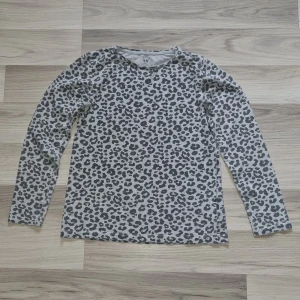 Leopardmönstrad långärmad tröja från H&M - Säljer en långärmad tröja från H&M i grått med svart leopardmönster. Tröjan är tillverkad i ekologisk bomull och har en klassisk, normal passform. Perfekt för dig som gillar djurmönster och vill ha något bekvämt och stilrent.