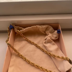 Guldigt cordell halsband - Säljer ett snyggt halsband i guld med tvinnad kedja. Perfekt accessoar för att lyfta din outfit med en elegant touch. Kommer i en tygpåse för förvaring.