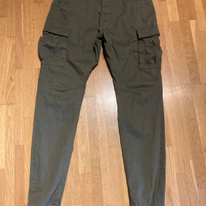 Olivgröna cargobyxor med fickor - Säljer ett par olivgröna cargobyxor med stora fickor på sidorna. Byxorna har stretch