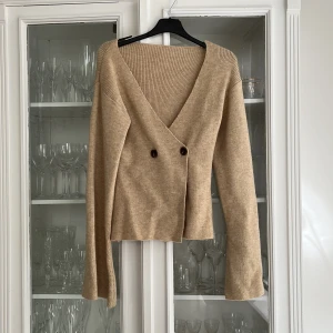 Beige omlott kofta med knappar - Köp via instabox!!! Säljer en beige stickad omlottkofta med v-ringning och två bruna knappar framtill. Koftan har långa ärmar och är tillverkad i ett mjukt, ribbat material. Den är aldrig använd endast testad!!