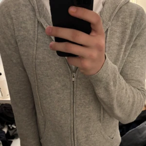 Ljusgrå stickad hoodie från John Brown - Säljer en ljusgrå stickad hoodie från John Henric med dragkedja framtill och huva med snören. Tröjan har långa ärmar och två fickor framtill. Perfekt för en avslappnad stil.