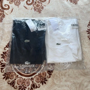 Storlek S på båda  - Klassisk svart t-shirt från Lacoste med rund hals och den ikoniska krokodilloggan broderad på bröstet. Tillverkad i mjuk bomull och har en normal passform. Perfekt för en stilren och enkel look.