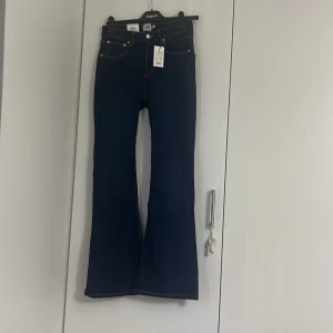 Mörkblå Snake Flare jeans med utsvängda ben - Säljer ett par mörkblå Snake Flare jeans från 157 med hög midja och utsvängda ben. Klassisk femficksmodell med kontrastsömmar och snygg passform. Perfekta för dig som gillar retrostil och vill ha något som sticker ut. Storlek M/short med snygga sömn detaljer. Aldrig använd helt nya, prislappen sitter. Original pris 300 