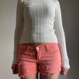 Lågmidjade korallrosa jeansshorts - Säljer ett par lågmidjade korallrosa jeansshorts från Cubus med fransig kant och slitna detaljer. Shortsen är i väldigt bra skick då de knappt använts. Skriv om ni undrar nåt!