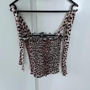 Leopardmönstrad smockad linnetopp från Gina Tricot - Säljer en leopardmönstrad smockad linnetopp från Gina Tricot. Toppen har breda knytband på axlarna och är elastisk i materialet. Perfekt för dig som gillar djurmönster och vill ha en trendig topp till sommaren.