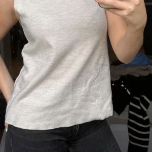 Ljusgrå ärmlös polotopp - Säljer en ljusgrå ärmlös polotopp i ribbat material. Toppen har en hög polokrage och är perfekt att styla med jeans eller kjol. Enkel och stilren design som passar till många tillfällen.