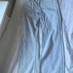Ljusblå raka jeans - Säljer ett par ljusblå jeans med rak passform och klassisk femficksdesign. Jeansen har normalhög midja och stängs med dragkedja och knapp. Perfekta till vardags för en avslappnad stil.