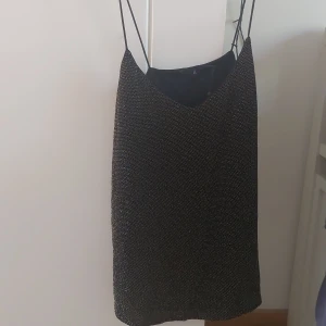 Svart glittrig topp med tunna axelband från Å - Säljer en svart glittrig topp med tunna axelband från Å. Toppen har en enkel och stilren design med lätt v-ringning och är perfekt för dig som gillar att sticka ut lite extra. Passar till många olika tillfällen!