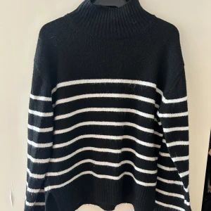 Svart och vit randig polotröja från Gina Tricot - Säljer en svart stickad polotröja från Gina Tricot med vita horisontella ränder. Tröjan har hög krage och långa ärmar, perfekt för kyligare dagar. Klassisk och enkel design som passar till mycket.