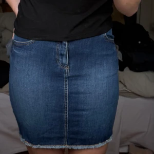 Blå jeanskjol med rå kant - Säljer en klassisk blå jeanskjol med fem fickor och rå, fransig kant nertill. Kjolen har normal passform och är i stretchigt denimtyg. Perfekt att matcha med en enkel t-shirt eller hoodie.