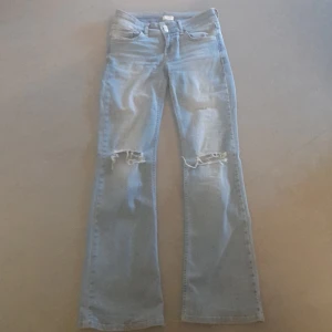 Ljusblå bootcut jeans från Nelly - Ljusblå jeans från Nelly med bootcut passform och slitna detaljer vid knäna. Klassisk femficksmodell med dubbla silverfärgade knappar framtill. Perfekta för en avslappnad och trendig look. Storlek 36. De är lite slitna längst ner men inget som syns bra, blir alltid så hur som helst efter 2-3 användningar.
