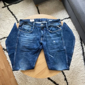 Klassiska standard Replay jeans - Tjena👋 säljer dessa klassiska blå Replay jeans med raka ben och knappgylf👖. Jeansen har slitningar och en något tvättad look, fem fickor och tydliga Replay-detaljer som läderpatch bak och röd etikett på bakfickan🧶 Byxorna har Anbass modell!  Jeansen är i storlek W34 L34!📐 Kom privat för mått!📏  Priset är INTE ristat i sten så kom gärna med prisförslag!💸  Vid frågor: Skicka ett meddelande📩