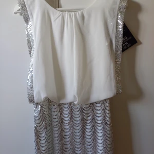 Vit paljettklänning från Model Behaviour - Säljer en vit klänning från Model Behaviour i storlek XS. Klänningen har glittriga paljettdetaljer längs sidorna och på kjolen, samt ett löst sittande liv. Perfekt för dig som vill sticka ut med en elegant och glittrig look.