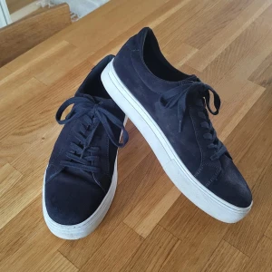Marinblå sneakers från Vagabond - Snygga marinblå sneakers från Vagabond med en stilren design. Skorna har en vit sula och snörning framtill. Perfekta för en avslappnad stil. De är bara andvända runt 5 gånger, köpte de för 1200kr. Kontakta mig om ni undrar nått 