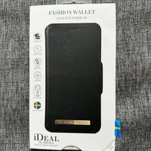 Svart plånboksfodral från iDeal of Sweden - Snyggt svart plånboksfodral till iPhone XR från iDeal of Sweden. Fodralet har en elegant gulddetalj med logga på framsidan och plats för kort på insidan. Perfekt för dig som vill ha både skydd och stil till mobilen. Finns defekter som kan ses på bilderna!