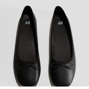 Svarta ballerinaskor med rosett från H&M - Klassiska svarta ballerinaskor från H&M med rund tå och en söt liten rosett framtill. Skorna har en enkel och stilren design som passar till många olika outfits.