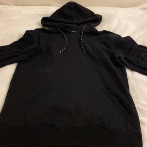 Svart hoodie från Axel Arigato med yin-yang brodyr - Säljer en svart hoodie från Axel Arigato med broderad yin-yang-symbol på bröstet. Tröjan har huva med dragsko och klassisk känguruficka framtill. Perfekt för en avslappnad och stilren look. Finns också en liten svart japansk text fram vid bröstet som inte syns så bra ‼️ Lappen med storleken fanns inte vid kragen och var lite gömd men det är M på storleken 😀