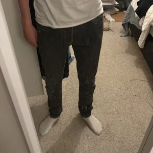 Svarta jeans från NN07 - Snygga svarta jeans från NN07 med klassisk femficksdesign och knappgylf. Perfekta för en stilren look. Storlek 29x32. En liten defekt på innerfickan (se bild 4-5) men annars i bra skick