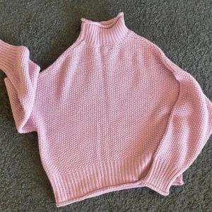 Rosa stickad tröja från First Class - Mysig rosa stickad tröja från First Class med hög krage och grovstickad struktur. Tröjan har långa ärmar och breda ribbade muddar vid ärmslut och nederkant. 