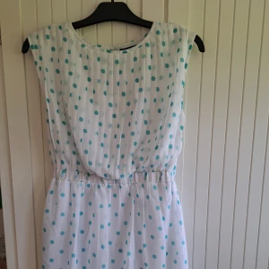 Vit prickig kortklänning från UNIQ - Superfin vit kortklänning från UNIQ med turkosa prickar och plisserad framsida. Klänningen har en avslappnad passform och är ärmlös, perfekt för varma dagar. Söt och lekfull stil som sticker ut!