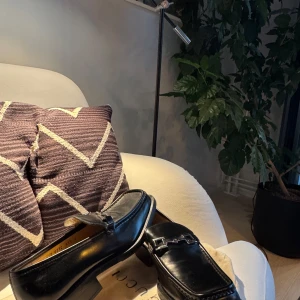 Svarta loafers från Gucci i skinn - Klassiska svarta loafers från Gucci i blankt skinn med ikonisk metallspänne framtill. Snygg, tidlös design med låg klack och rund tå. Perfekta för dig som vill ha en stilren och lyxig look. Nypris 11 tusen!