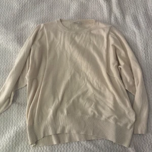 Beige stickad tröja från KappAhl - En stilren beige stickad tröja från KappAhl i storlek M. Tröjan har rund halsringning, långa ärmar och breda ribbade muddar vid ärmslut och nederkant. Perfekt för lager-på-lager och enkel att matcha med jeans eller kjol.