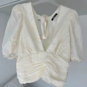 Vit omlottopp med puffärm - Säljer en vit omlottopp från Gina Tricot med djup v-ringning, knyt i ryggen och puffiga korta ärmar. Toppen har ett tunt, lätt strukturerat tyg och fina volangdetaljer framtill. Storleken motsvarar mer M