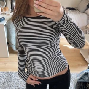 Svartvit randig långärmad topp - Säljer en svartvit långärmad topp med smala horisontella ränder. Tröjan har rund djupare ringning bak. Figurnära passform och mjukt, stretchigt material. Perfekt till jeans eller kjol!