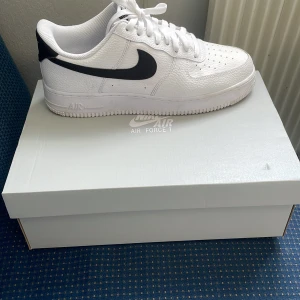 Nike Air Force 1 i vitt och svart (44) - Säljer ett par klassiska Nike Air Force 1 sneakers i vitt skinn med svart swoosh. Skorna har snörning, rund tå och platt sula. Perfekta för dig som gillar stilrena och tidlösa sneakers. Storlek 44. Har aldrig använt dem bara hemma när jag skulle testa dem. Säljer pågrund av att jag ska köpa andra skor