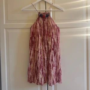 Mönstrad kortklänning från Zara - Superfin kortklänning från Zara med rosa och beige batikmönster. Klänningen har tunna axelband och coola färgglada stenar vid halsringningen. Luftig modell som passar perfekt till varma dagar. Materialet känns lätt och flowy.
