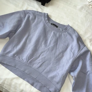 Ljuslila croppad sweatshirt från Zara - Superfin ljuslila croppad sweatshirt från Zara med rund hals och breda muddar vid ärmslut och nederkant. Tröjan har en relaxed fit och är gjord i mjuk bomullsblandning, perfekt för en chill och trendig look.