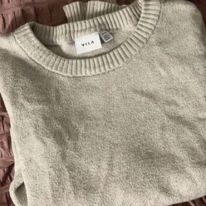 Beige stickad tröja från VILA - Mysig beige stickad tröja från VILA med rund halsringning och ribbade muddar. Perfekt för lager-på-lager och enkel att matcha med jeans eller kjol. Klassisk modell med lång ärm och mjukt material som känns skönt mot huden.
