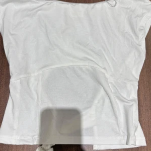 Vit omlottopp med knyt från Gina Tricot - Supersnygg vit omlottopp från Gina Tricot i storlek XS. Toppen har en cool öppen detalj i midjan och knytning på sidan som ger en trendig look. Tillverkad i mjuk bomull, perfekt till jeans eller kjol när du vill sticka ut lite extra.