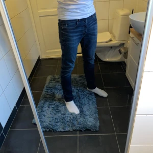 Blåa jeans från G-Star RAW - Säljer ett par snygga blå jeans från G-Star RAW med klassisk femficksdesign och läderpatch bak i midjan. Jeansen har tydliga slitningar och kontrastsömmar, sitter tight och har en modern look. Perfekta för dig som gillar en stilren och trendig vibe.