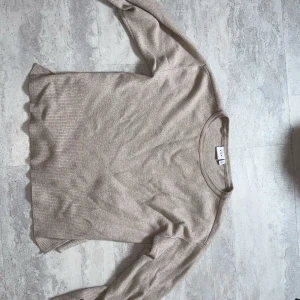 Beige stickad tröja från Arket - En stilren beige stickad tröja från Arket med rund halsringning och långa ärmar. Tröjan har en mjuk känsla och ribbade muddar vid ärmslut och nederkant. Perfekt för lager-på-lager och enkel att matcha med jeans eller kjol. Fraktas såklart strykt och nytvättad 