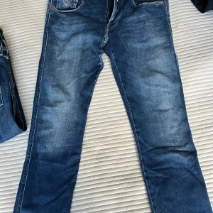 Replay Anbass jeans blå herr 31/32 - Säljer ett par snygga Replay Anbass jeans i klassisk blå tvätt. Jeansen har raka ben, fem fickor och diskreta slitningar för en cool look. Tillverkade i stretchigt jeanstyg som sitter skönt hela dagen. Perfekta för dig som gillar stilrena och bekväma jeans.