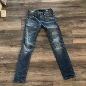 Replay Anbass slim fit jeans blå - Snygga blå Replay Anbass jeans i slim fit med klassisk femficksdesign och läderpatch bak. Jeansen har en lätt tvättad look med slitningar och är tillverkade i mjukt denimtyg. Perfekta för dig som gillar en smalare passform och stilren design. Storlek är 29 midja och 34 längd 