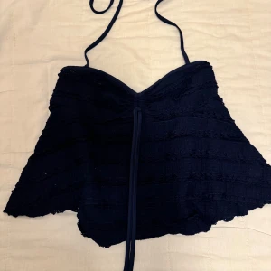 Marinblå croppad linnetopp med knyt - Säljer en marinblå croppad linnetopp med tunna axelband och knyt framtill. Toppen har en lätt volangig kant nertill och är perfekt för varma dagar. (Ser mörkare ut på bild) 