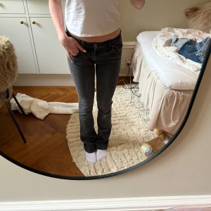 Svarta bootcut jeans - Säljer ett par svarta bootcut jeans med klassisk femficksdesign och låg midja. Jeansen har en snygg tvätt och sitter tight upptill med utsvängda ben. Perfekta för dig som gillar en tidlös och enkel stil.