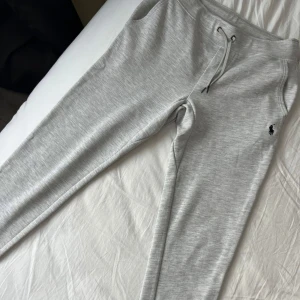 Grå mjukisbyxor Polo Ralph Lauren - Snygga ljusgrå mjukisbyxor från Polo Ralph Lauren med klassisk broderad logga på höften. Byxorna har dragsko i midjan och är tillverkade i mjukt bomullsmaterial. Perfekta för chill eller träning.