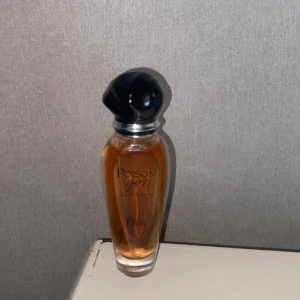 Dior Poison Girl Eau de Toilette - Dior Poison Girl Eau de Toilette i en elegant, smal glasflaska med persikofärgad vätska. Flaskan har en svart, rundad kork och silverdetaljer. Parfymen har en feminin och modern design som sticker ut på hyllan. Endast testad